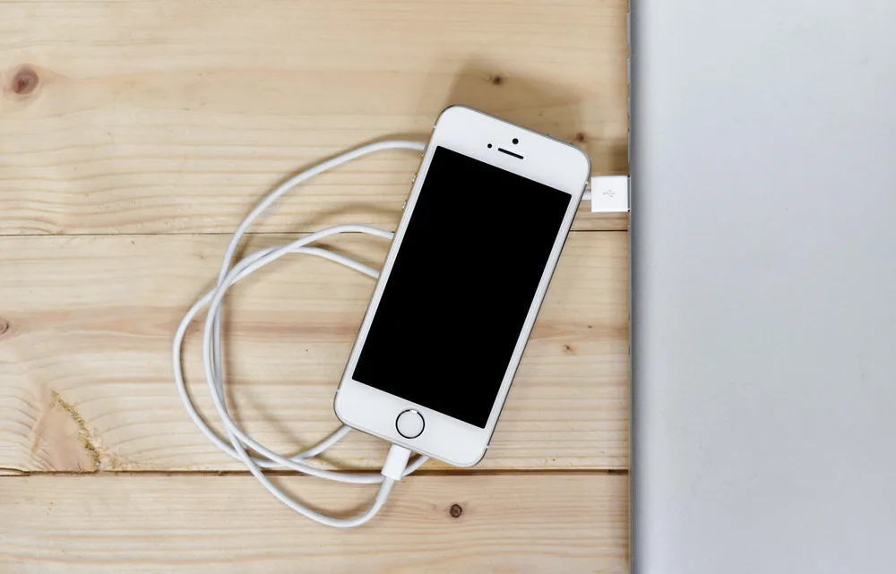 A phone charging on a wooden dock on a clean desk