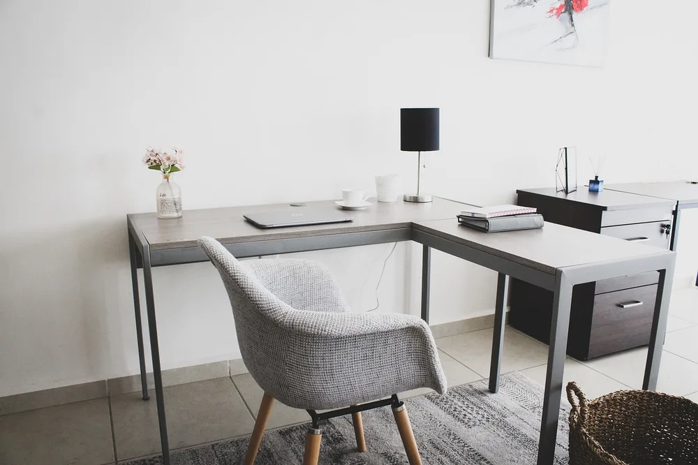 A cozy small home office with a slim desk, shelves, a plant and a lamp